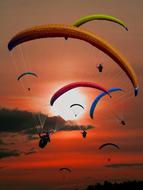 multi-colored paragliders on a background of red sunset