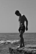 black and white photo of a man on a stone near the sea