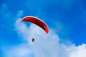 man on a red paraglider against a cloudy sky