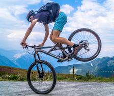 Biker, doing trick on the road, on the colorful and beautiful mountains, under the blue sky with white clouds