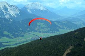 Paragliding, Paraglider flying above green forested mountain side at scenic landscape