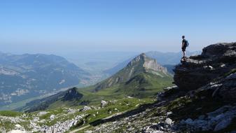climber stands on a cliff in the background of the Alpine Valley