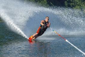 Man in glasses, doing water skiing, on the water with ripple, near the green plants