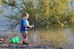 Child fishing on the beautiful shore with stones and green plants