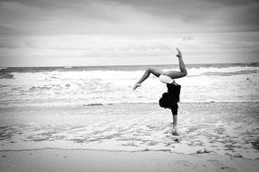 Gymnastics, Girl standing on hands at surf line on Beach