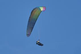 Person, doing paragliding with the beautiful and colorful parachute, at blue sky