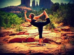 Woman balancing while doing yoga exercise, on the beautiful landscape on the rocks with green plants