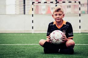 boy with a soccer ball sits on the background of the gate