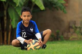 dark skin child Boy with Football sits on lawn