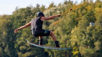 Person, jumping, while doing wakeboarding, near the beautiful and colorful trees