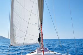 White sailboat, among the beautiful, blue waterscape with ripple, at blue, gradient sky on background