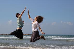 People, jumping on the beautiful beach with waves, at background with the sky with clouds