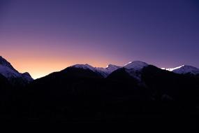 sun rising in purple sky behind snow-capped Mountains