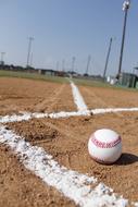 White and red baseball on the gravel, on the colorful field, at blue sky on background