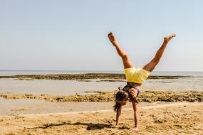 young Girl stands on hands on Beach