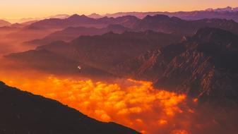 Person, doing paragliding, above the beautiful mountains, with the clouds, at colorful and beautiful sunrise, in Italy