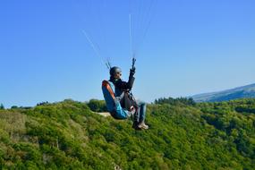 Paraglider at clean blue sky above green mountains