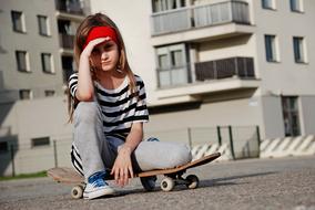 caucasian child girl sits on skateboard at house