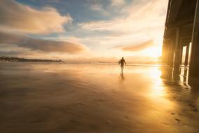 man with surfboard at sea during sunset