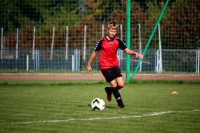 boy in red-black uniform trains on the football field