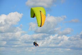 Paraglider with the green, orange and black parachute at blue sky with white clouds in France