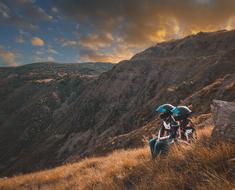 young boy and girl in Motorcycle helmets sit on grass at scenic mountain landscape