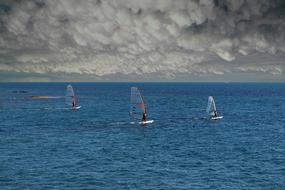 Colorful boats for windsurfing on the blue water of the ocean, under the cloudy sky