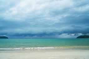 Beautiful landscape of the colorful water, under the cloudy sky, from the sandy beach