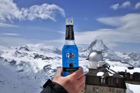 bottle with alcohol in a man's hand on the background of the Alps