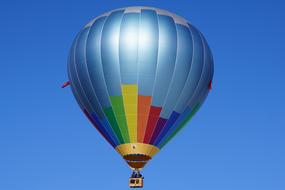 Flying, shiny, colorful, patterned hot air balloon, at blue sky on background, in Switzerland