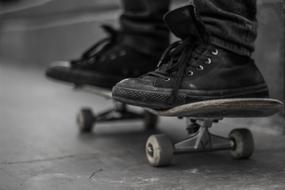 the legs of a guy in black sneakers on a skateboard