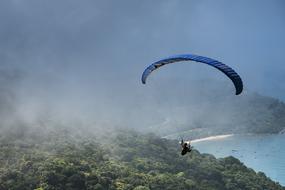 paraglider flying in fog above forest at coastline on the landscape