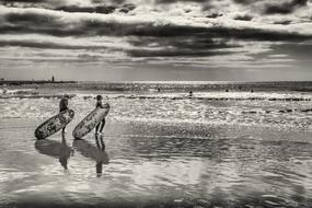 two Surfers walking on wet beach to Water