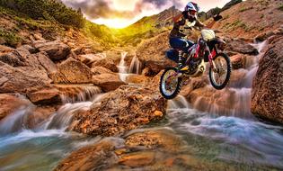 extreme stunt of a motorcyclist on the background of a cascade of a mountain rive