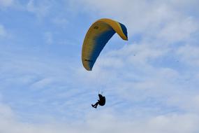 Paraglider on the beautiful and colorful, gradient Ozone Rush 5 Wing at blue sky with white clouds