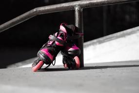 Pink and black inline skates near the railing, in the skate park, in light and shadow