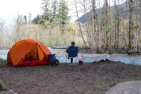 person sits beside of tent on riverside, usa, washington, olympic national park