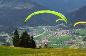 Flying green and white paraglider above the fields