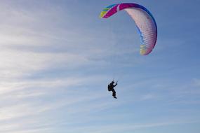 Person, doing paragliding with the colorful parachute, at blue sky with white clouds on background