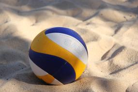 Beautiful, blue, yellow and white volleyball on the sand, in light