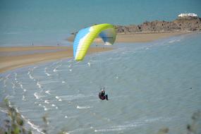 Person, doing paragliding on the beautiful, blue, white and green parachute, above the beautiful sandy beach
