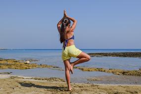 girl meditates on one leg on the seashore