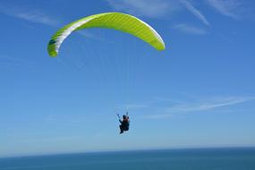 photo of an athlete with a green parachute against a blue sky over the sea in France