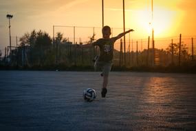 Boy, playing football on the court, at beautiful and colorful sunset