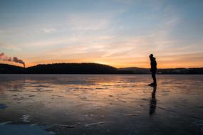 a man stands on ice on a lake during sunset