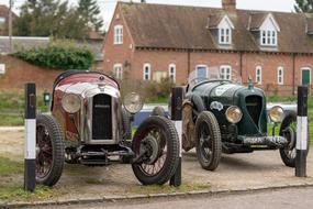 two Vintage Cars parked in front of old brick house