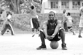 Black and white photo of the basketball player, sitting on the ball in Africa