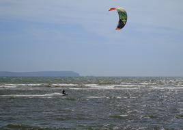 Person, surfing with the colorful kite, above the beautiful waterscape