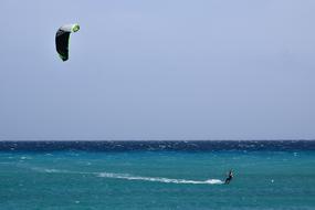 Person doing kitesurfing with the black and green parachute, above the green and blue water