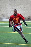 American football player, running on the green field, with yellow and white lines, with the ball